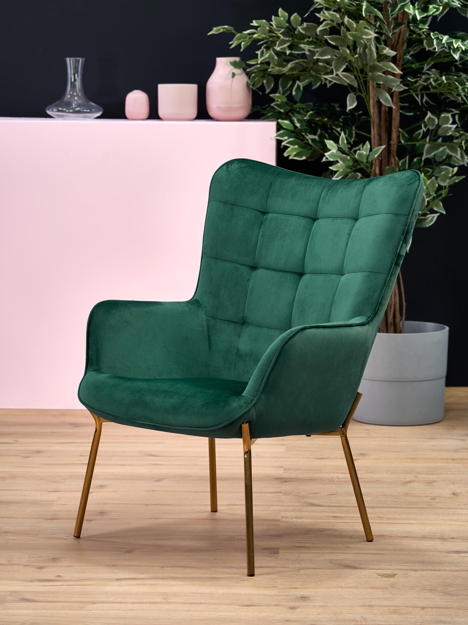 Zbliżenie na aksamitne obicie w ciemnozielonym fotelu CASTEL ze złotymi nogami.