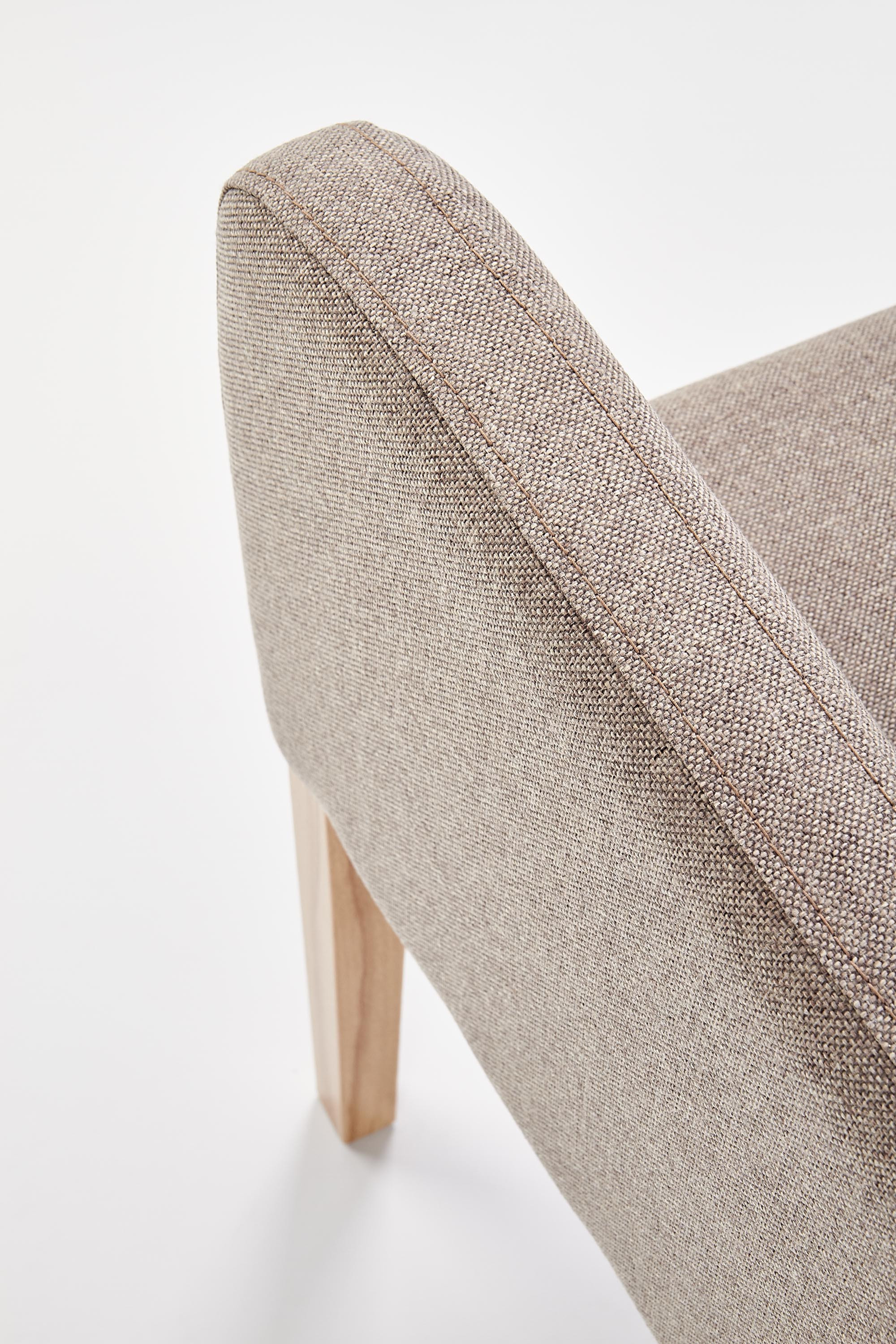 Zbliżenie na brązową tkaninę i drewnianą nogę fotela FILO w odcieniu dębu miodowego.