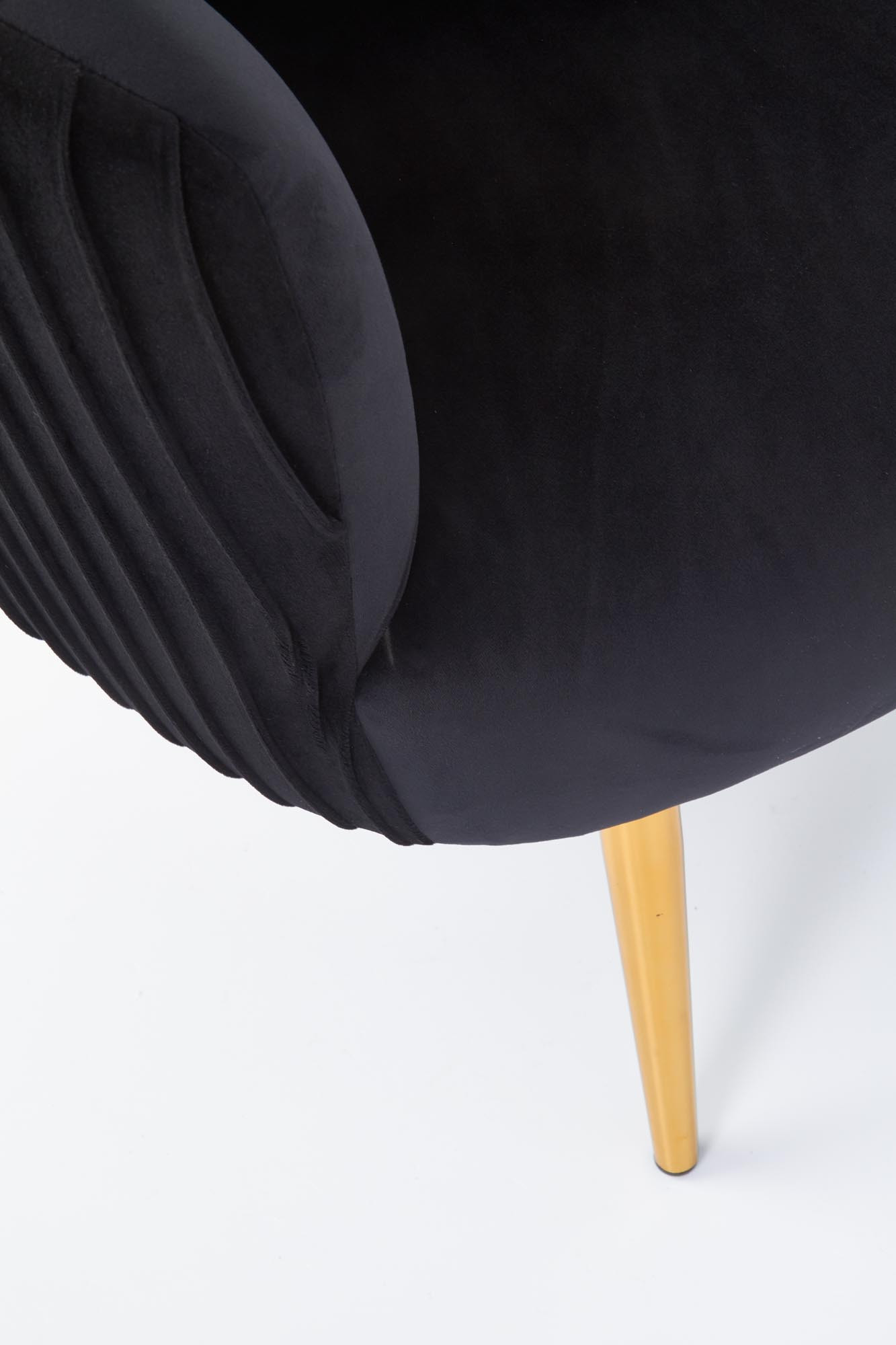 Zbliżenie na czarny welurowy fotel CROWN z plisowanym bokiem i złotą nogą.
