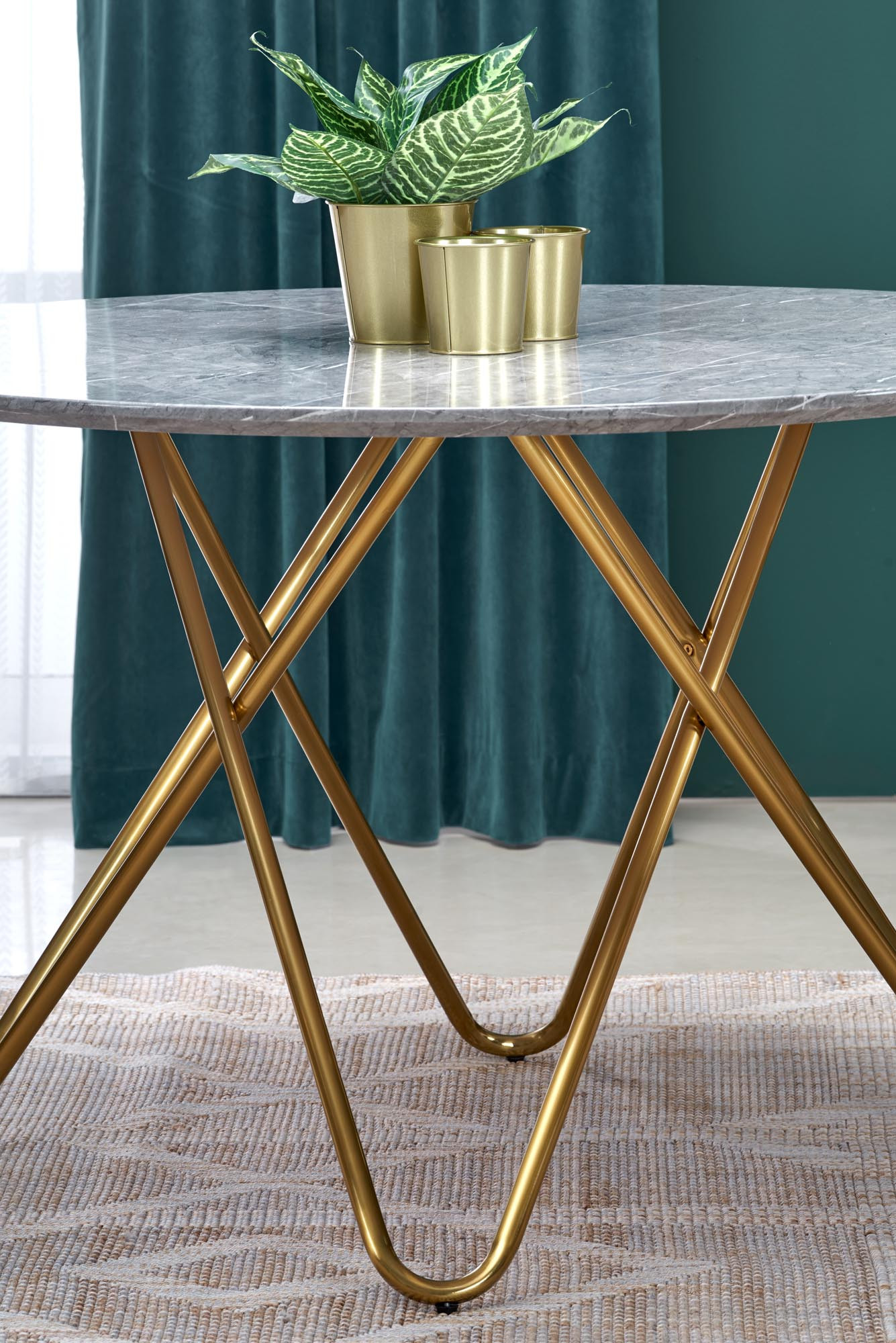 Okrągły stół z popielatym marmurowym blatem i złotymi, krzyżującymi się nogami – widok z przodu.