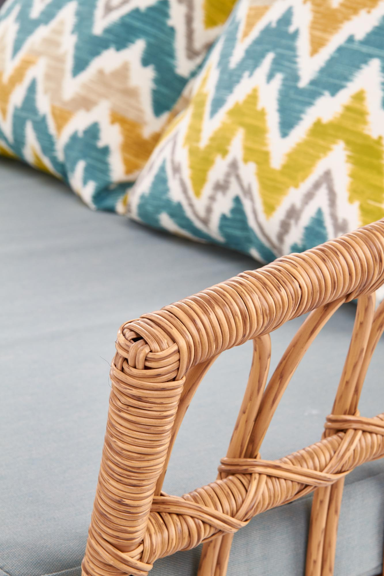 Zbliżenie na rattanowy podłokietnik sofy GARDENA z poduszkami w kolorowe zygzaki.