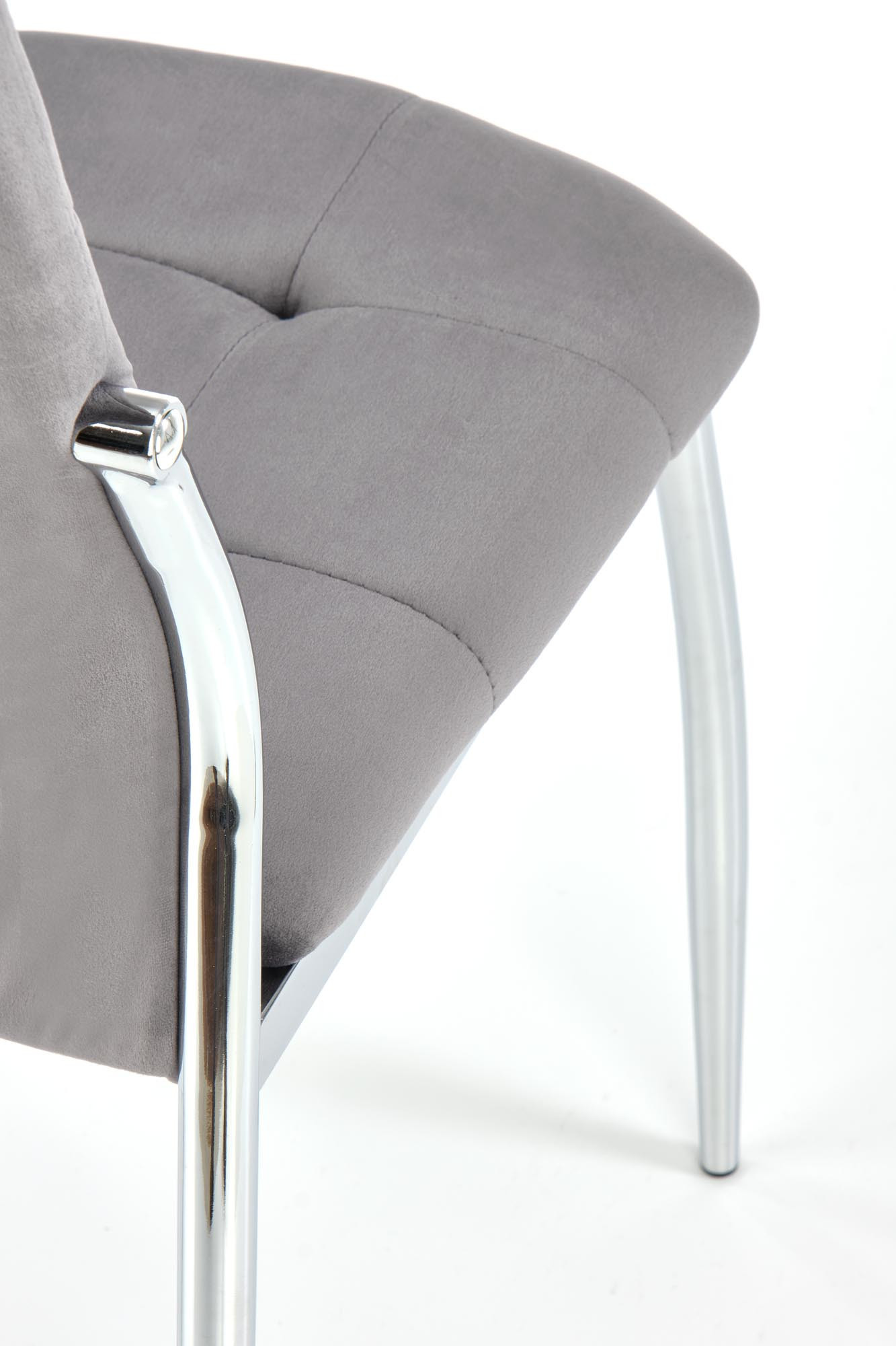 Zbliżenie na pikowane siedzisko i chromowane nogi krzesła K416 z popielatego weluru.