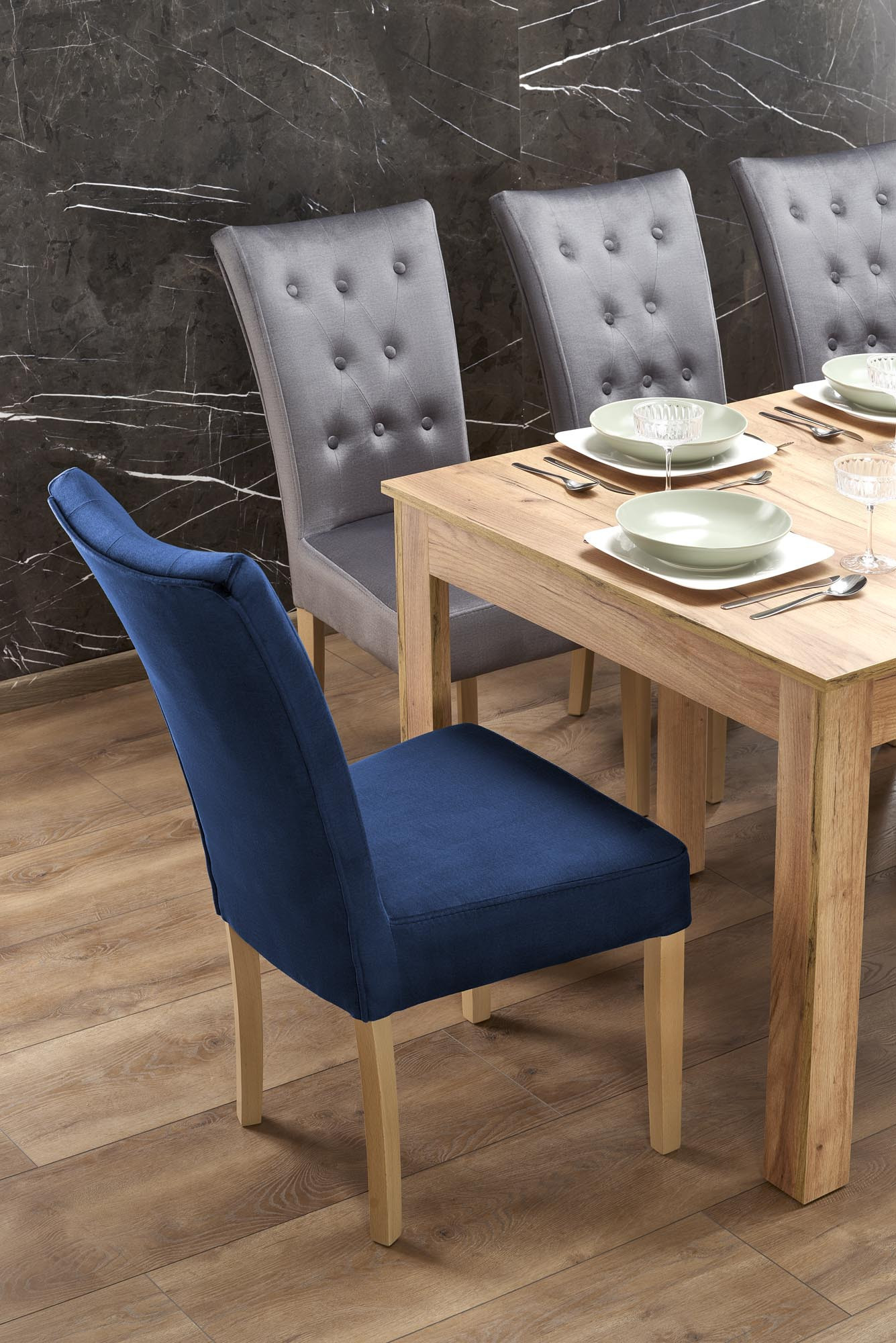 Widok z boku rozkładanego stołu SEWERYN z dębu craft oraz krzeseł w szarym i granatowym kolorze.