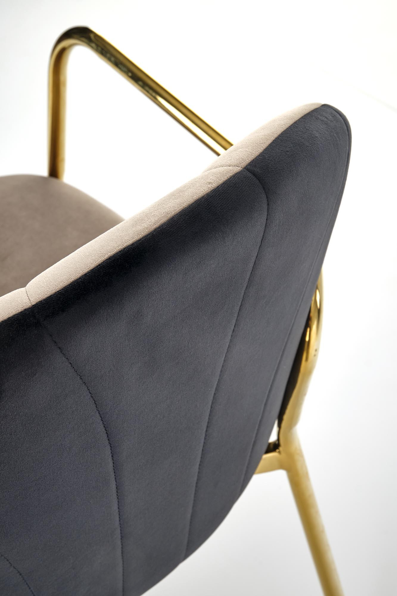 Zbliżenie na beżowo-czarne krzesło K500 z tapicerowaną muszlą i złotymi nogami.