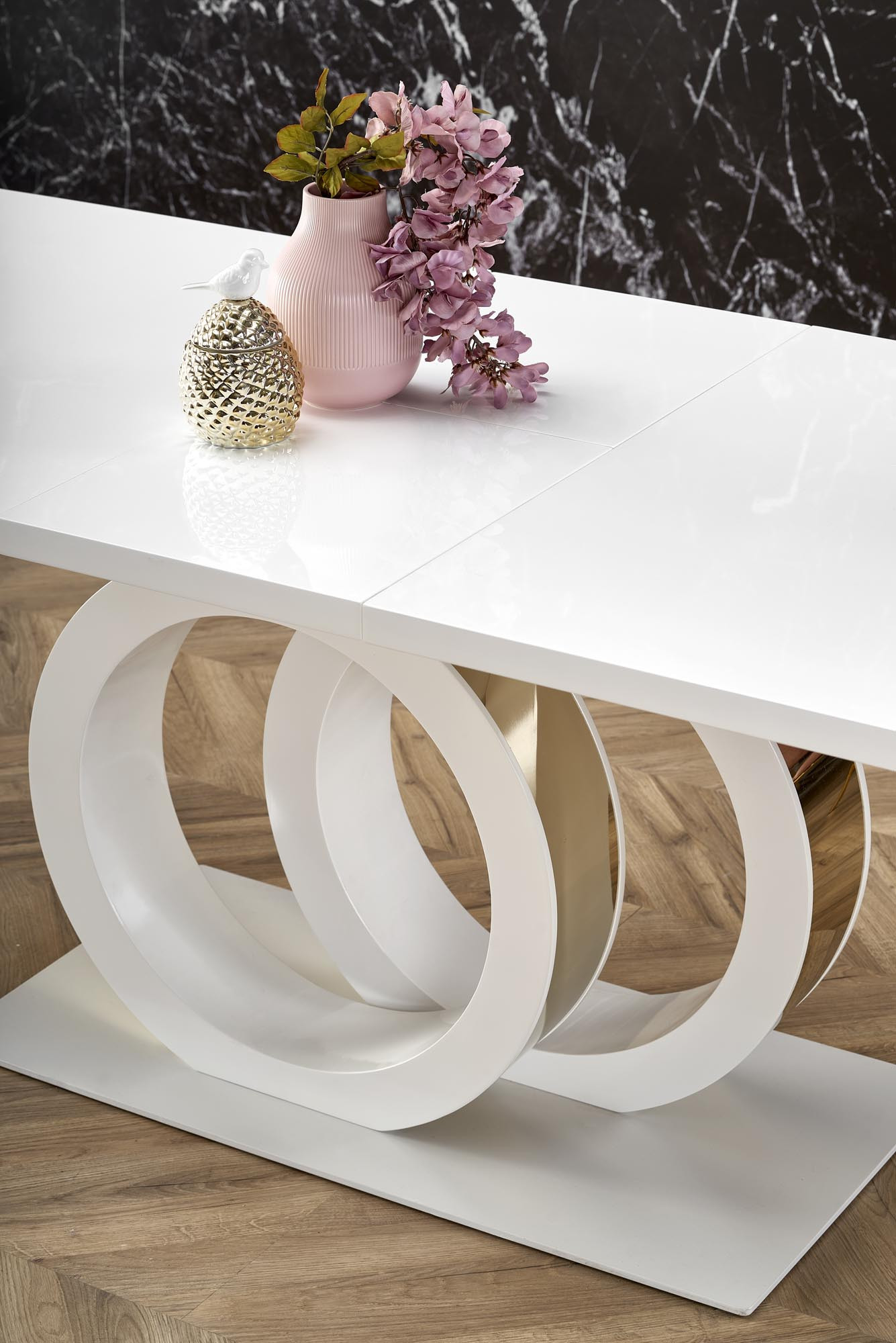 Zbliżenie na biało-złoty rozkładany stół GALARDO z dekoracją kwiatową i rzeźbioną podstawą w kształcie kół.