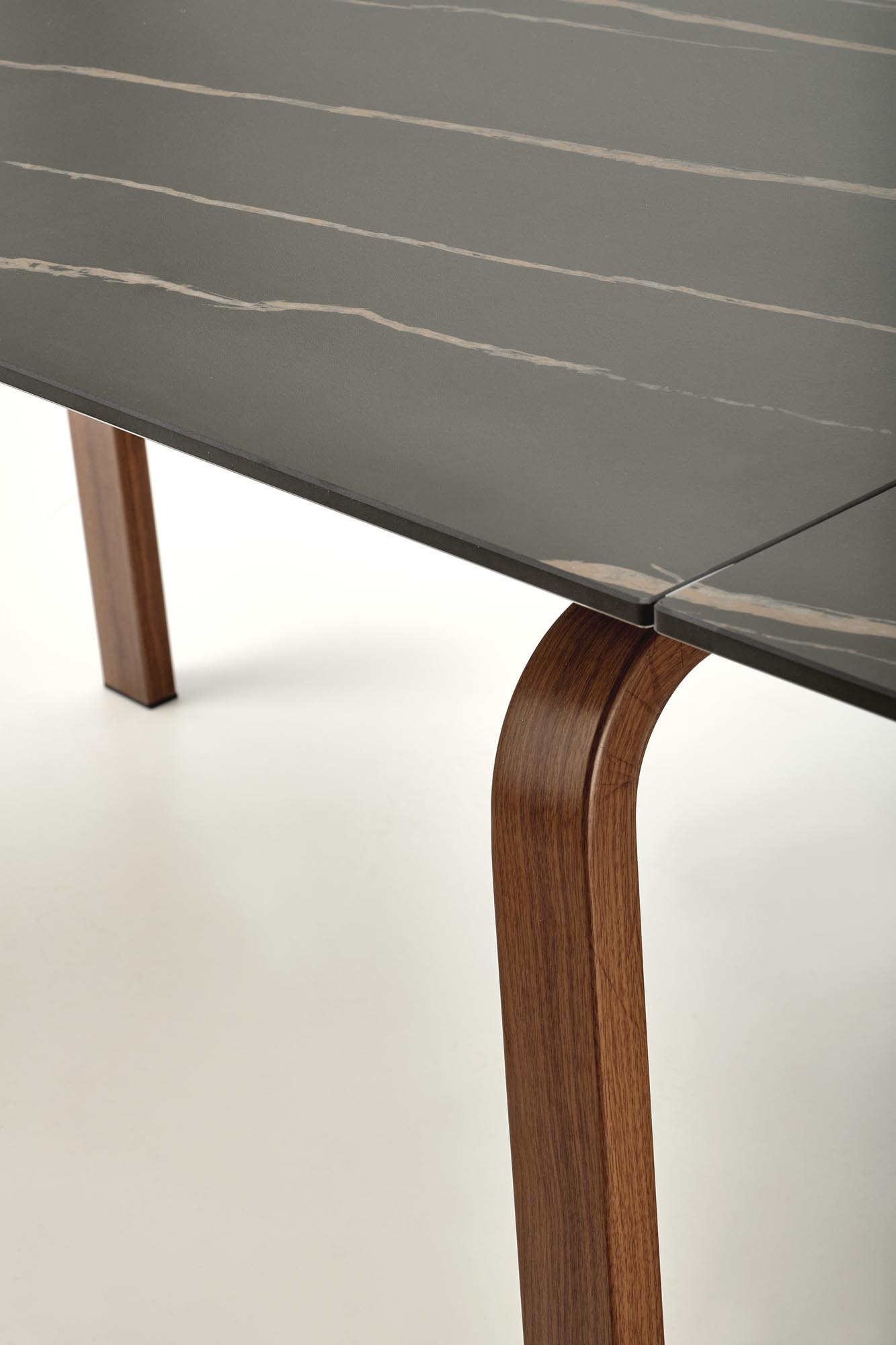 Zbliżenie na czarny marmurowy blat rozkładanego stołu z orzechowymi nogami.