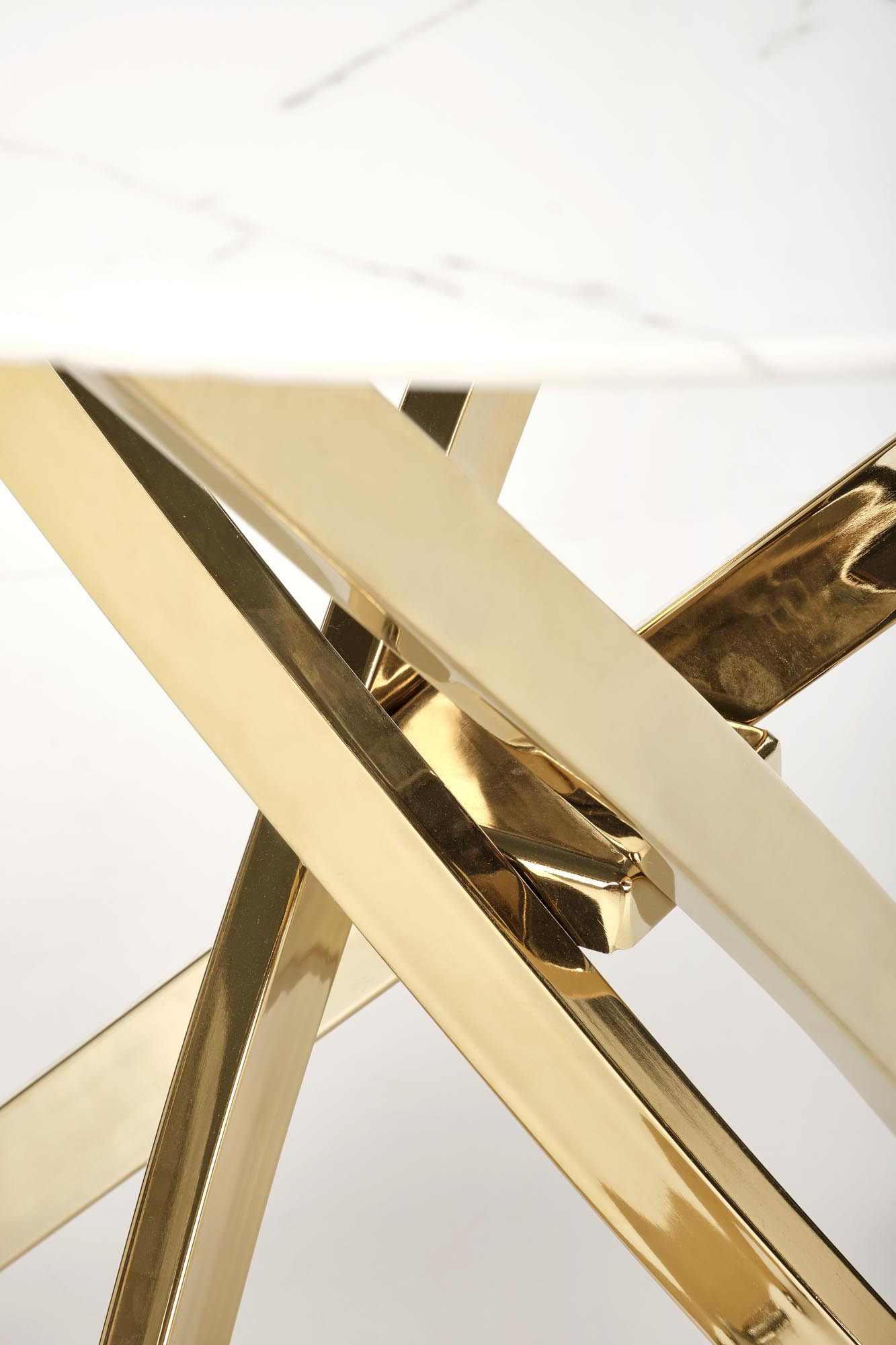 Zbliżenie na złote, krzyżujące się metalowe nogi okrągłego stołu z białym marmurowym blatem.