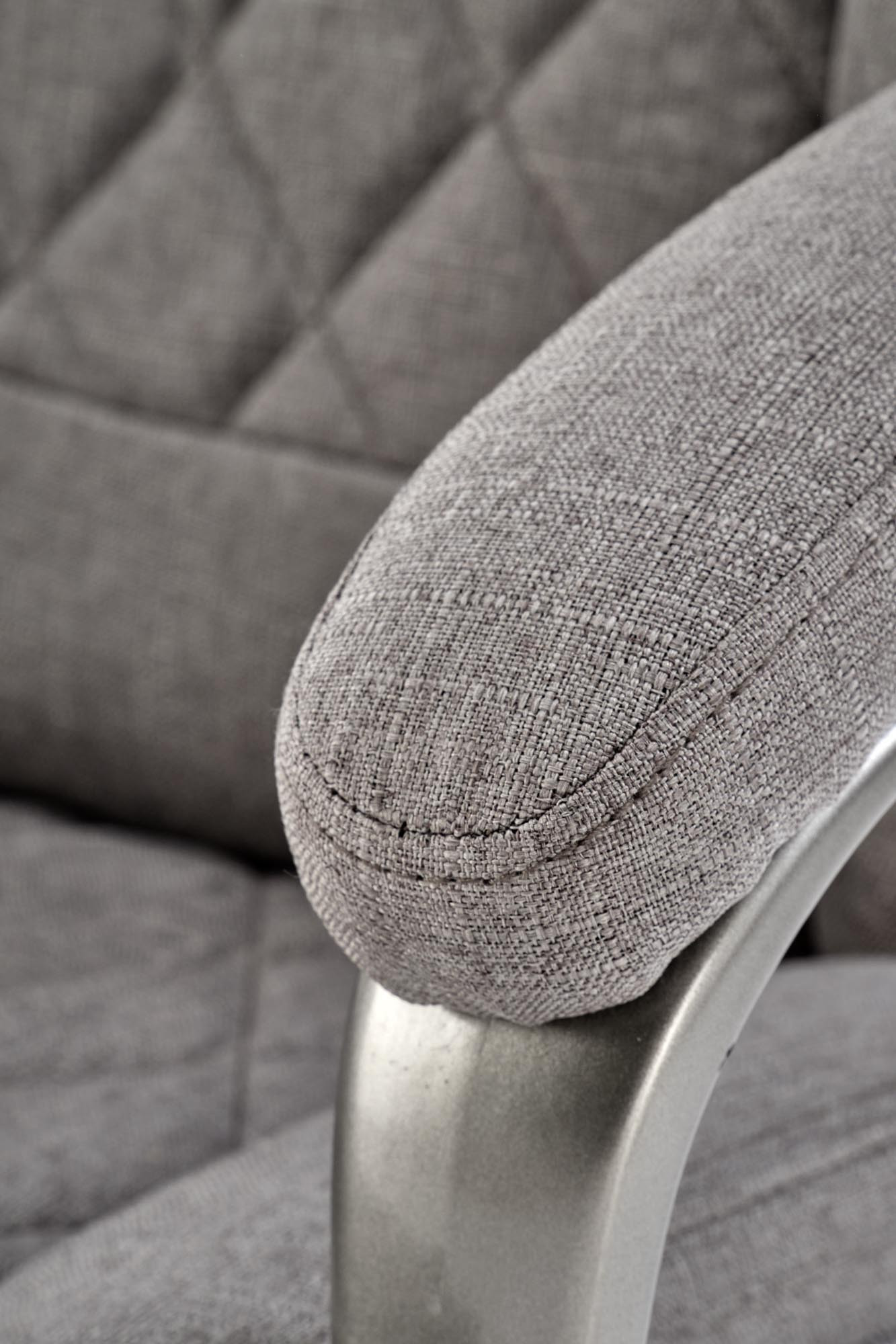 Zbliżenie na popielate, pikowane oparcie i podłokietnik fotela gabinetowego HELDER 2 z chromowanymi elementami.
