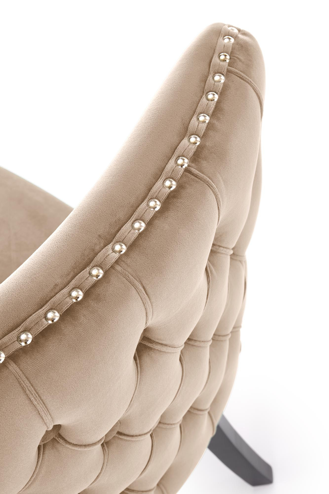 Zbliżenie na beżowy welurowy fotel ALDA z drewnianymi nogami i złotymi ćwiekami na bokach.