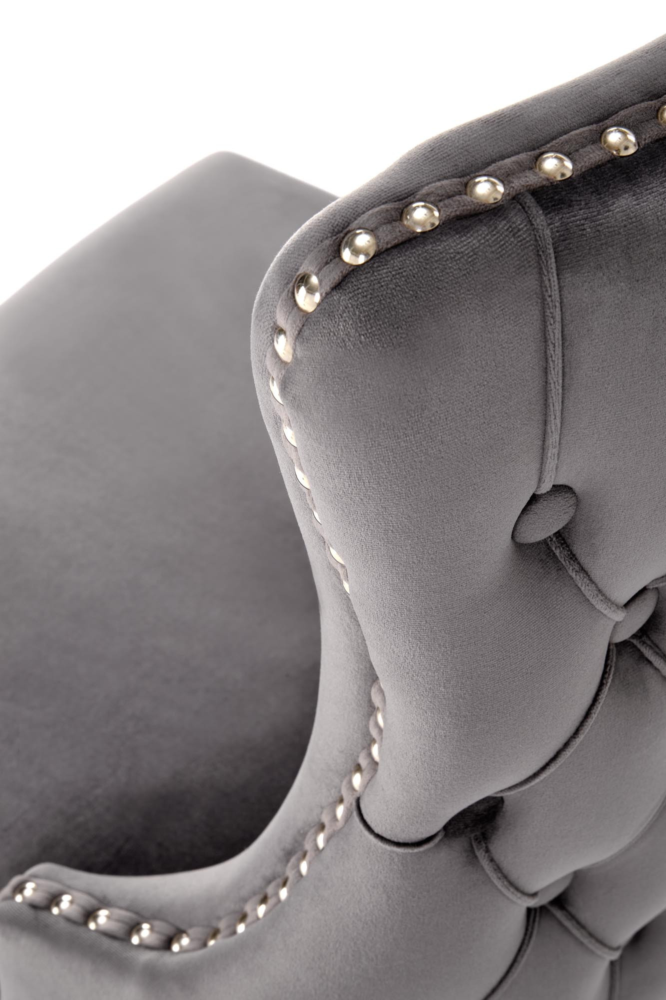 Zbliżenie na popielate krzesło ALDA z velvetu z drewnianymi nogami i złotymi ćwiekami na bokach.