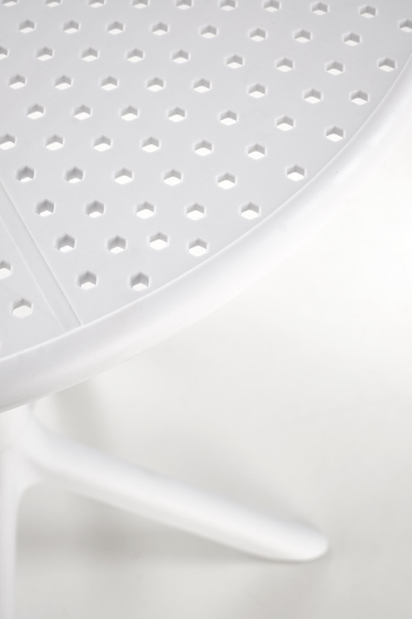 Zbliżenie na biały okrągły stół CALVO z polipropylenu z heksagonalnymi otworami na blacie.