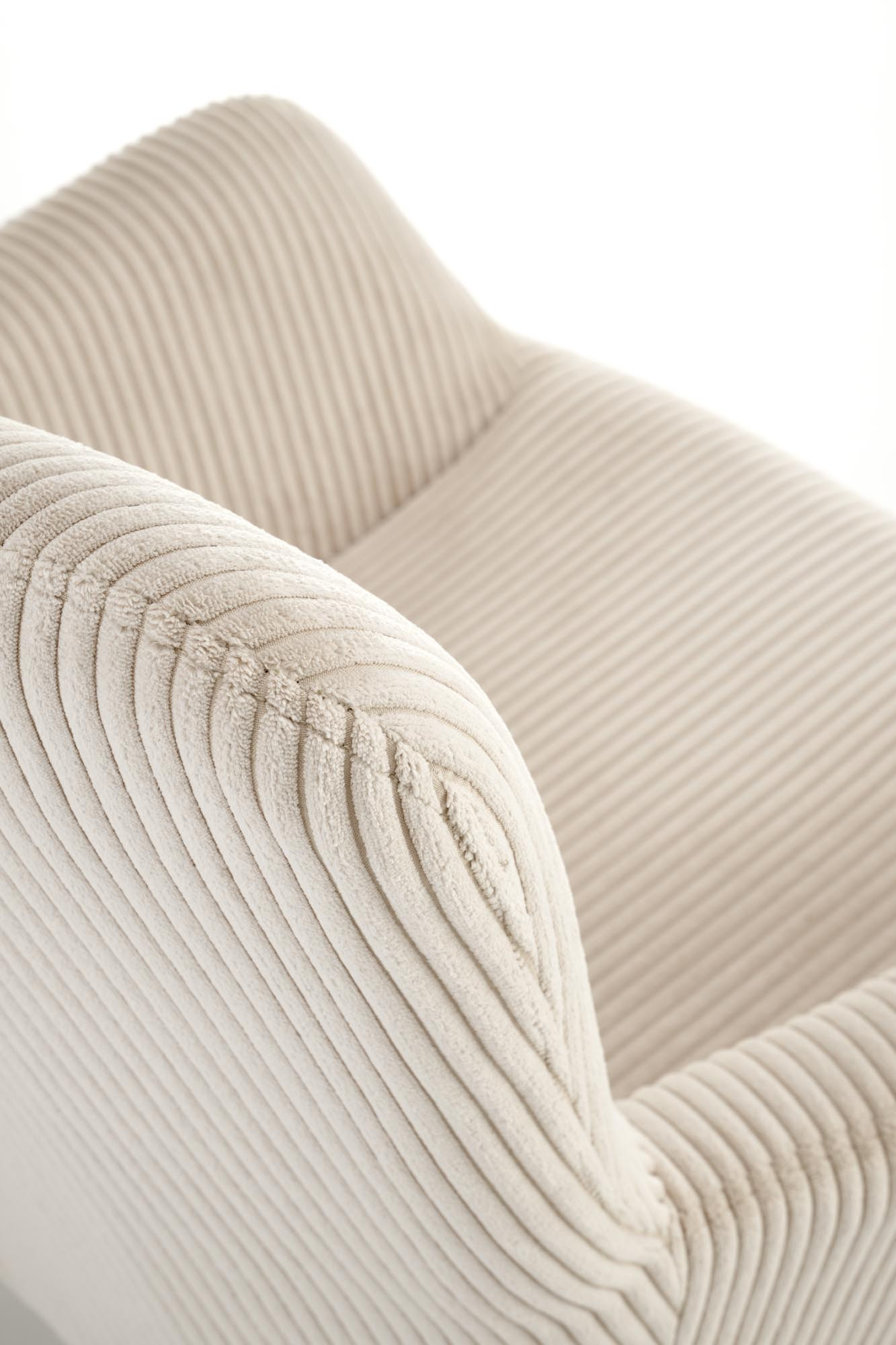 Zbliżenie na kremowy sztruksowy fotel wypoczynkowy AMARO z zaokrąglonym oparciem.