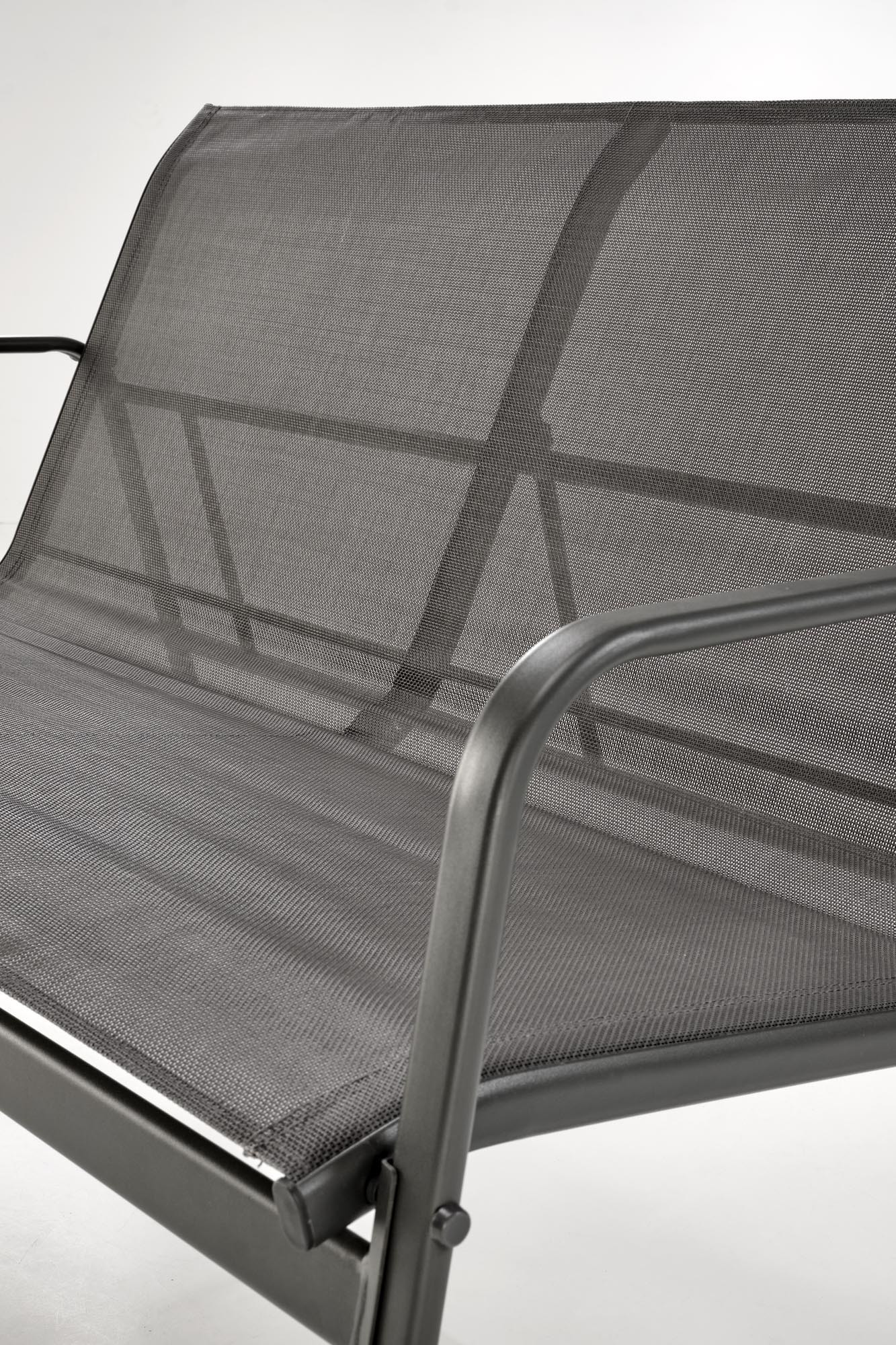 Zbliżenie na popielatą siatkową sofę ogrodową CONOR z metalowymi podłokietnikami.