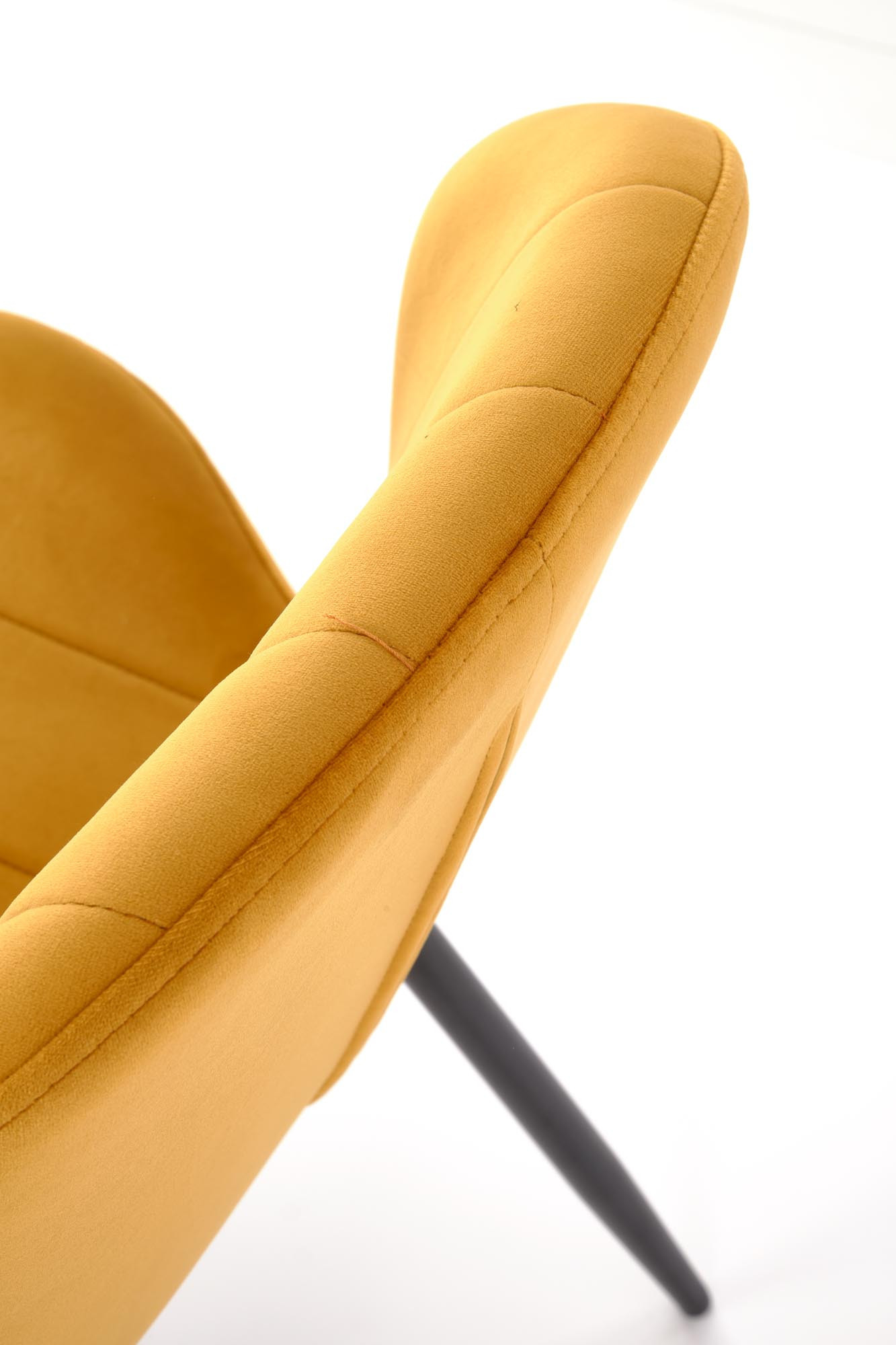 Zbliżenie na musztardowe, pikowane oparcie krzesła K538 z weluru i czarnymi stalowymi nogami.