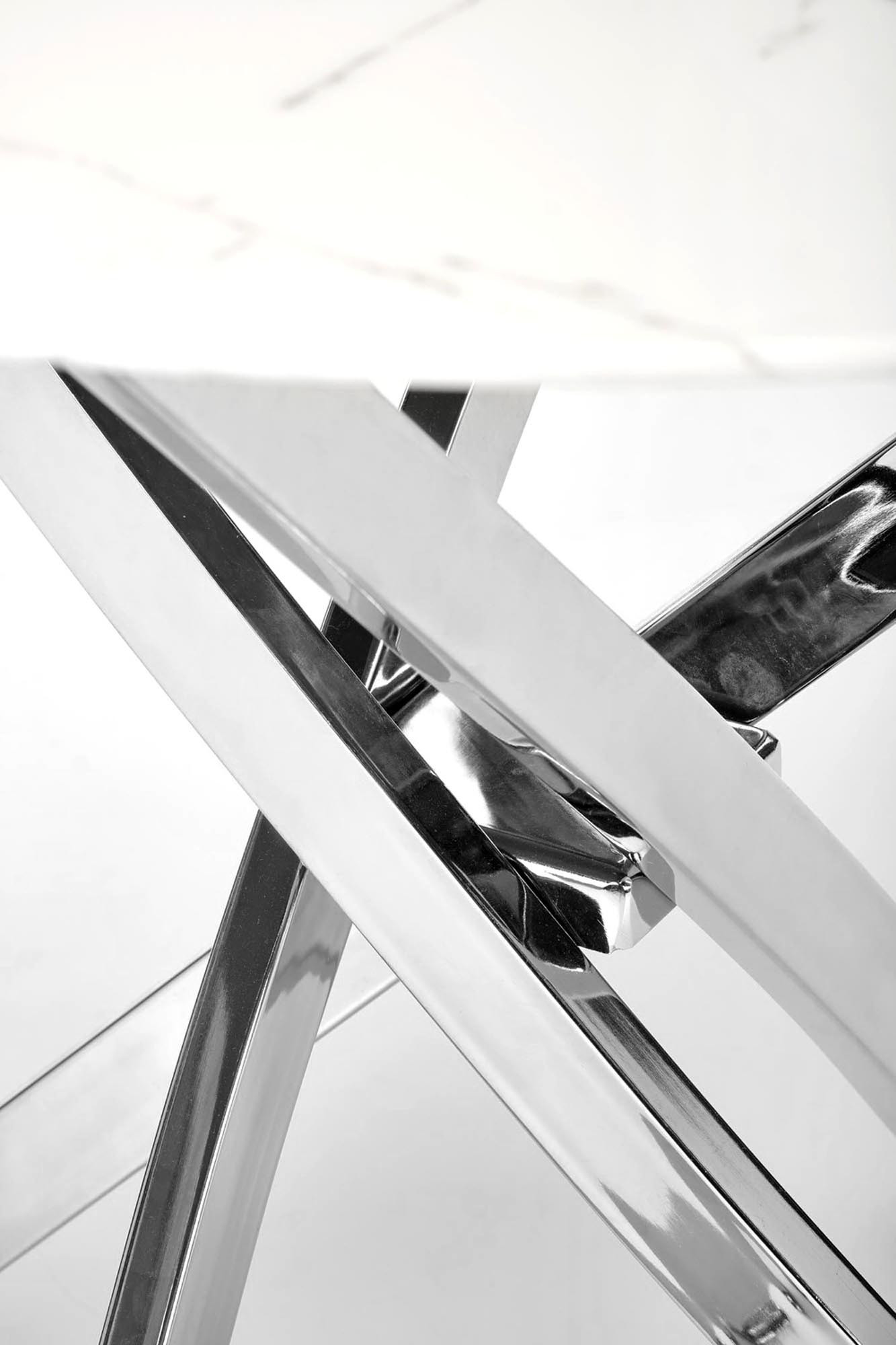 Zbliżenie na chromowane krzyżujące się nogi stołu ze szklanym blatem w marmurowym wzorze.