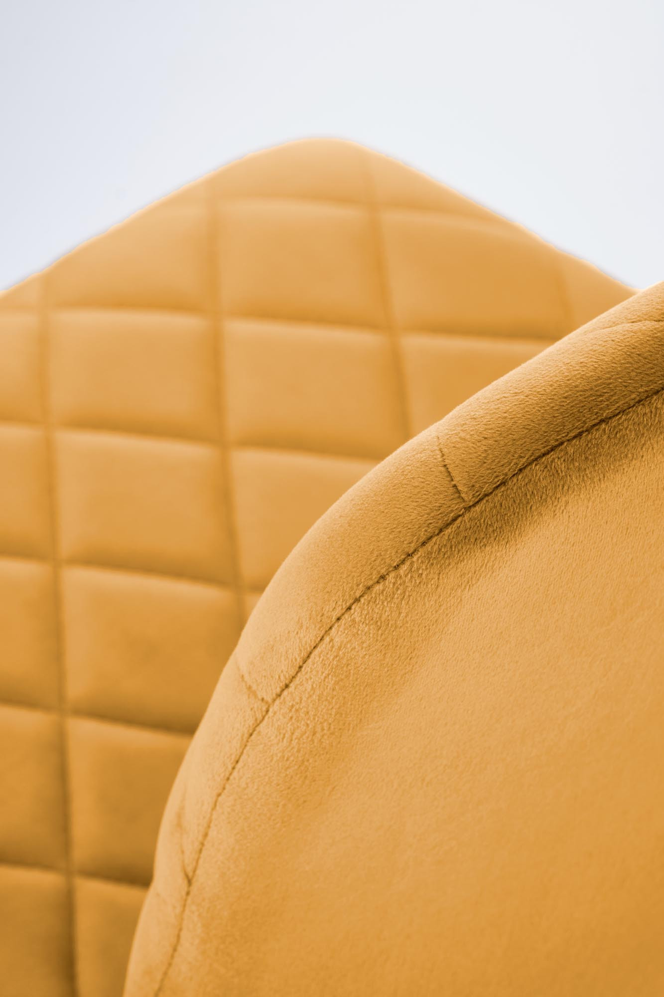 Zbliżenie na musztardowe krzesło K525 z pikowanym welurowym oparciem i stalowymi nogami.