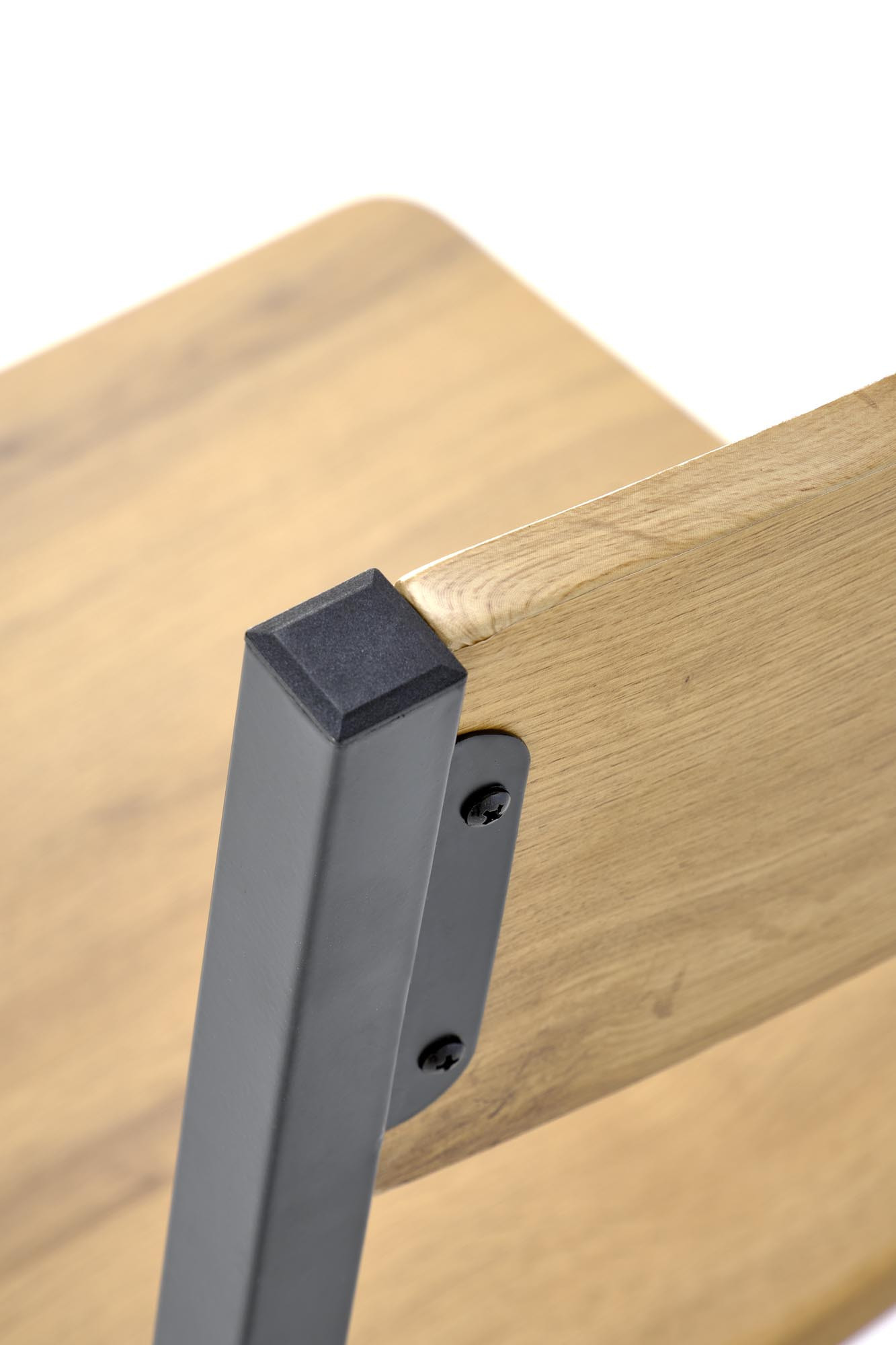 Zbliżenie na narożnik drewnianego siedziska krzesła MILTON z metalową ramą.