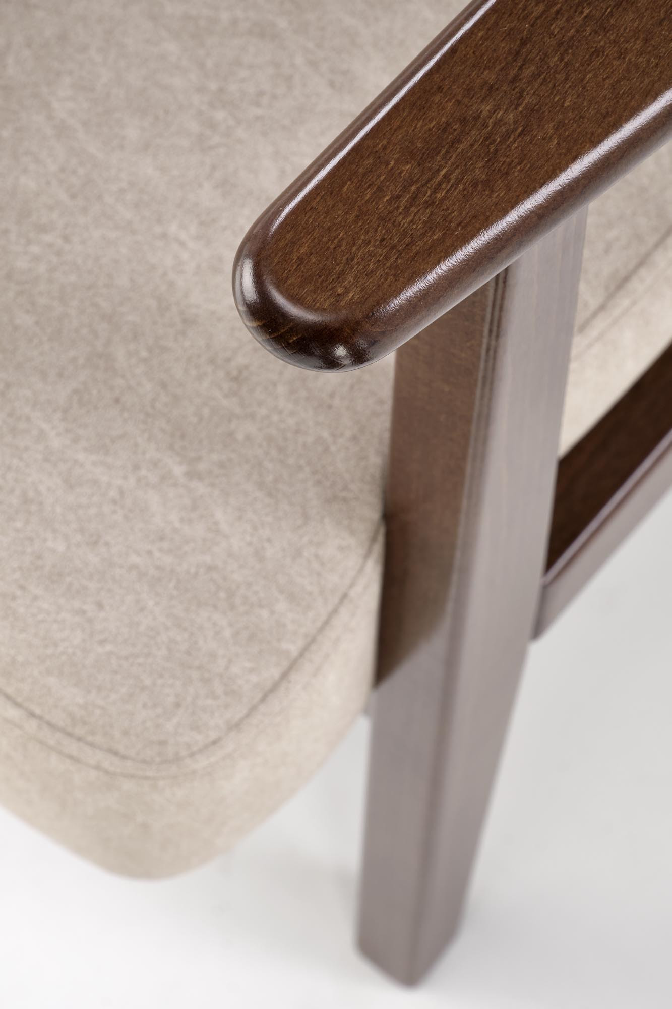 Zbliżenie na podłokietnik i siedzisko beżowego fotela MILANO 1S z ciemnymi bukowymi nogami.