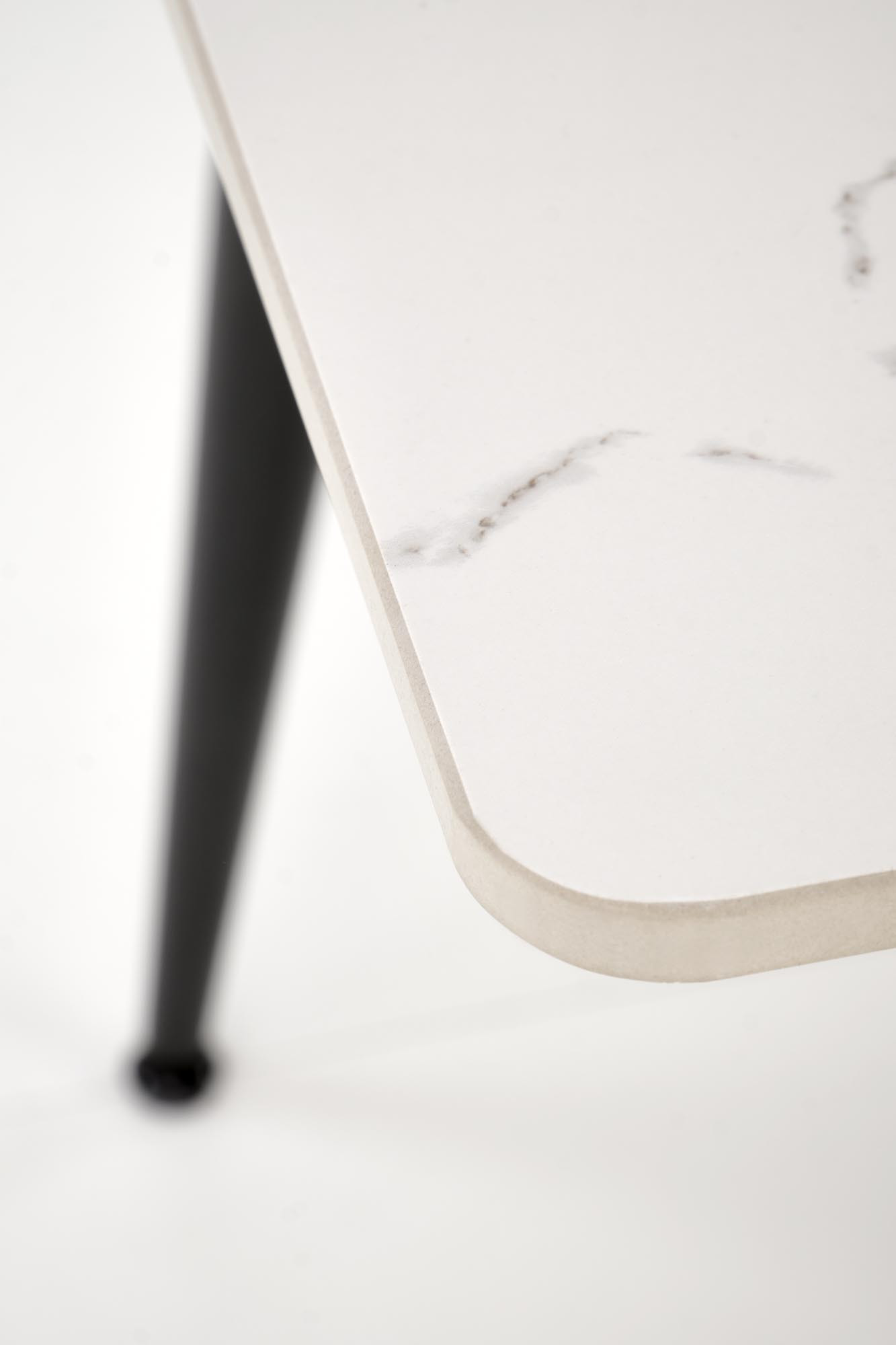 Zbliżenie na biały blat stołu EMILIO z delikatnymi szarymi żyłkami i czarną stalową nogą.