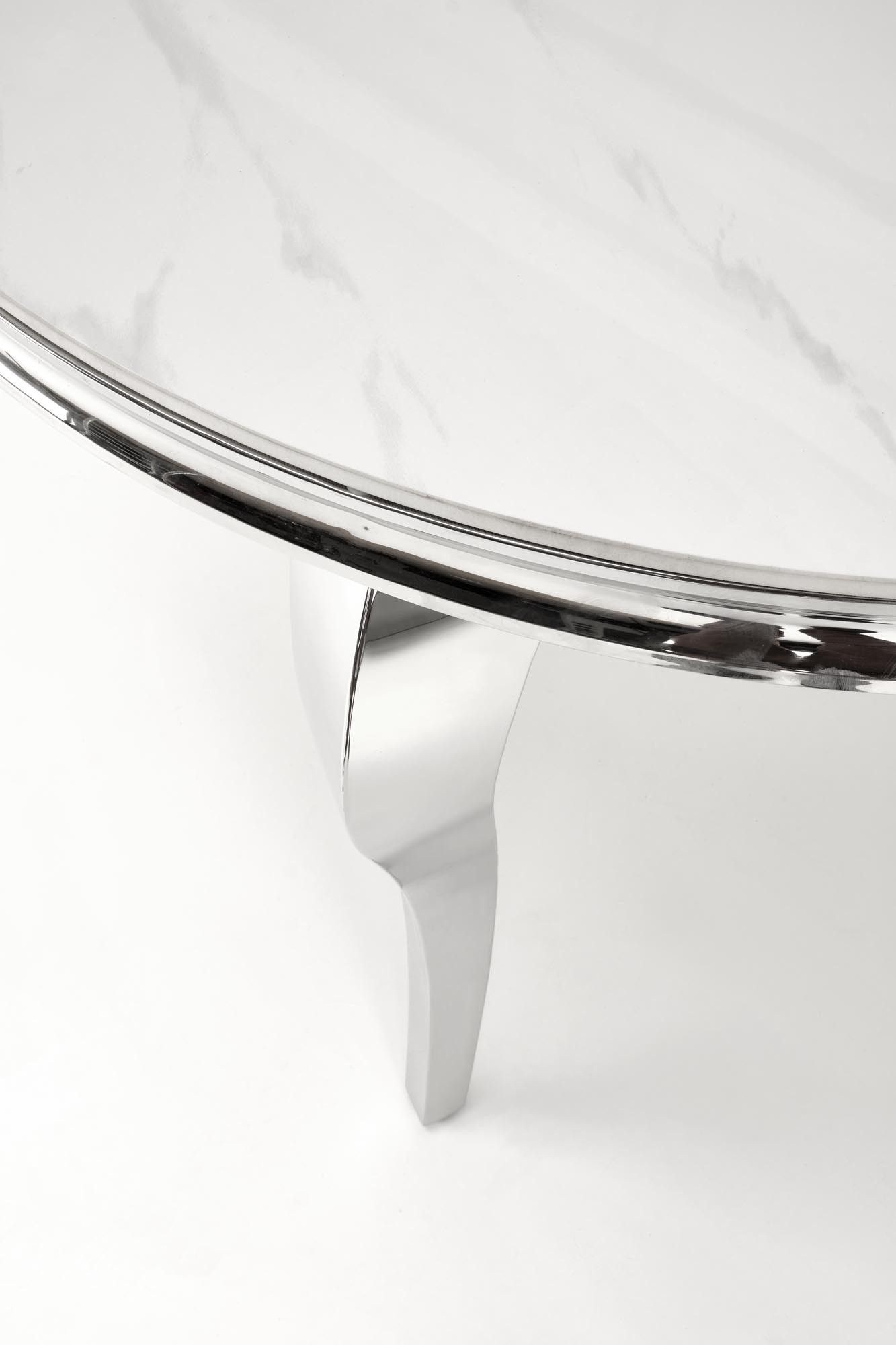 Zbliżenie na srebrną, zakrzywioną nogę stołu glamour z blatem imitującym biały marmur.