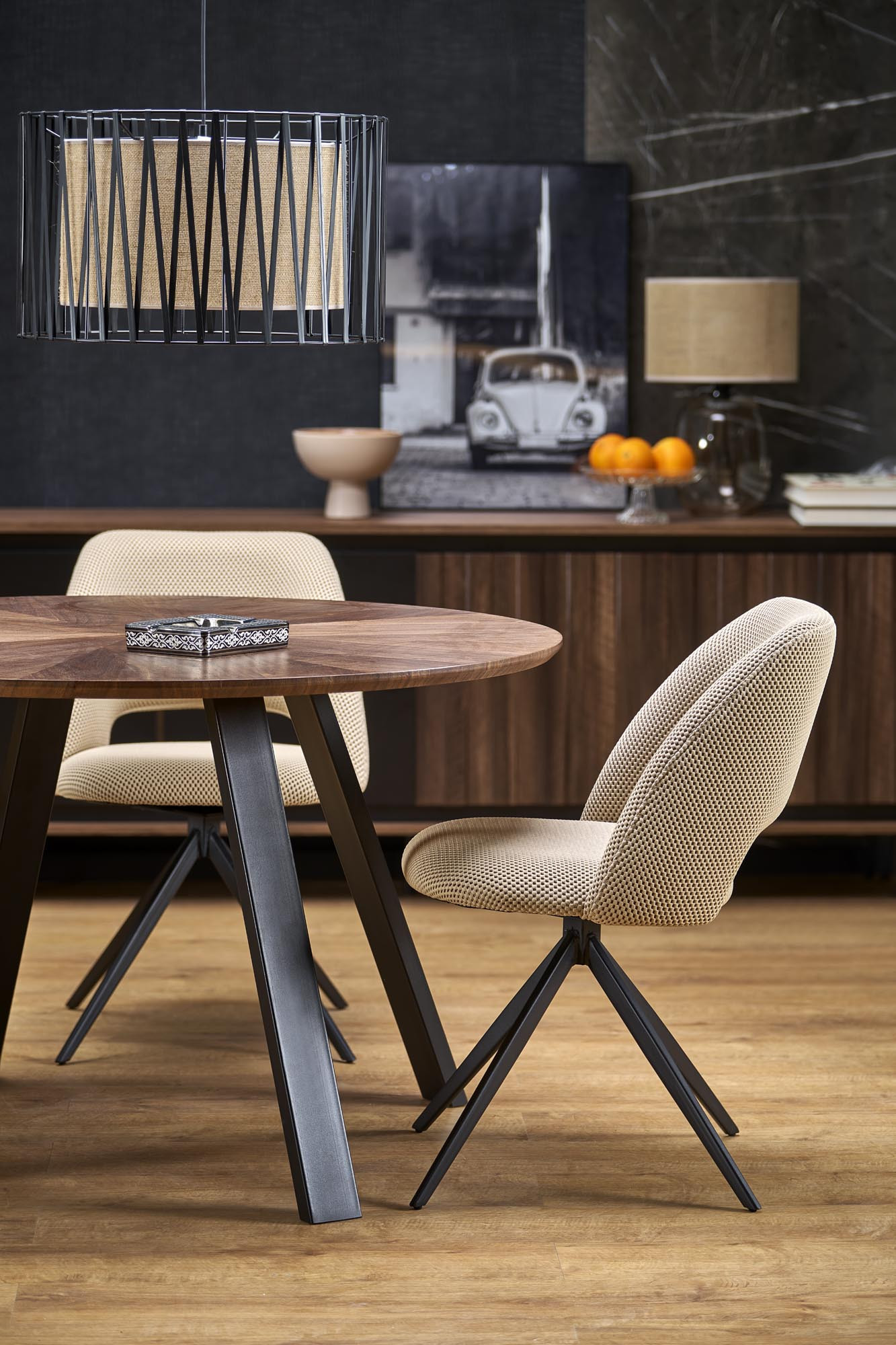 Okrągły stół DANILO z orzechowym blatem i stalowymi nogami – widok z boku, otoczony dwoma beżowymi krzesłami.
