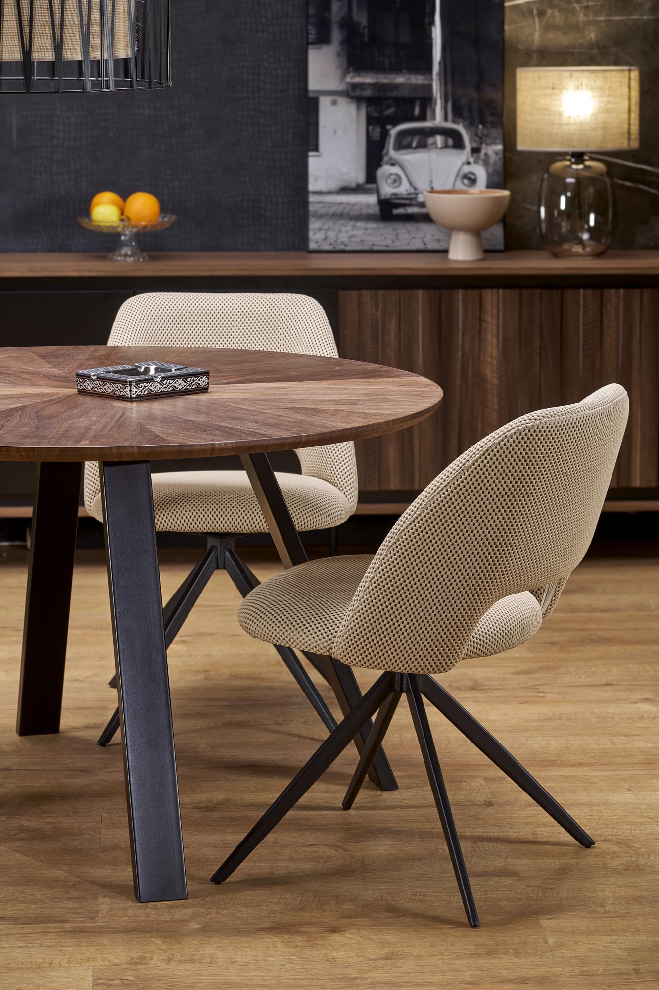 Okrągły stół DANILO z orzechowym blatem i stalowymi nogami – otoczony dwoma beżowymi krzesłami.